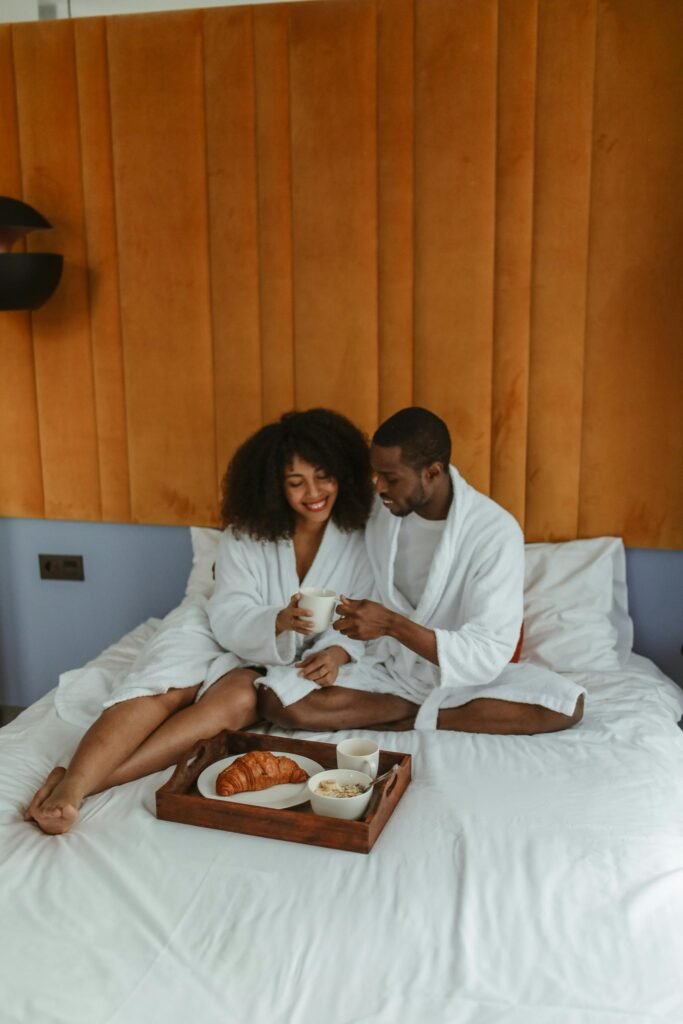 Couple enjoying breakfast in bed, smiling and embracing each other while holding coffee mugs.